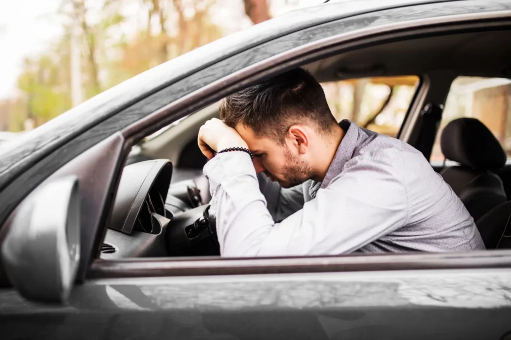 A distressed driver sitting in a car with his head in his hand